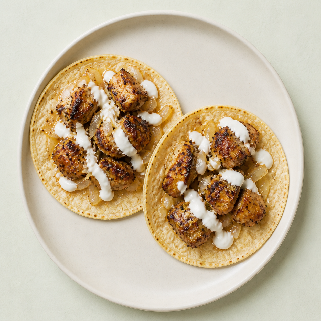 An overhead view of two smoky chicken tacos with onion and yogurt sauce